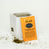 Orange wrapped sachet of Peppermint Leaves leaned againsy a small white block surrounded by loose peppermint.
