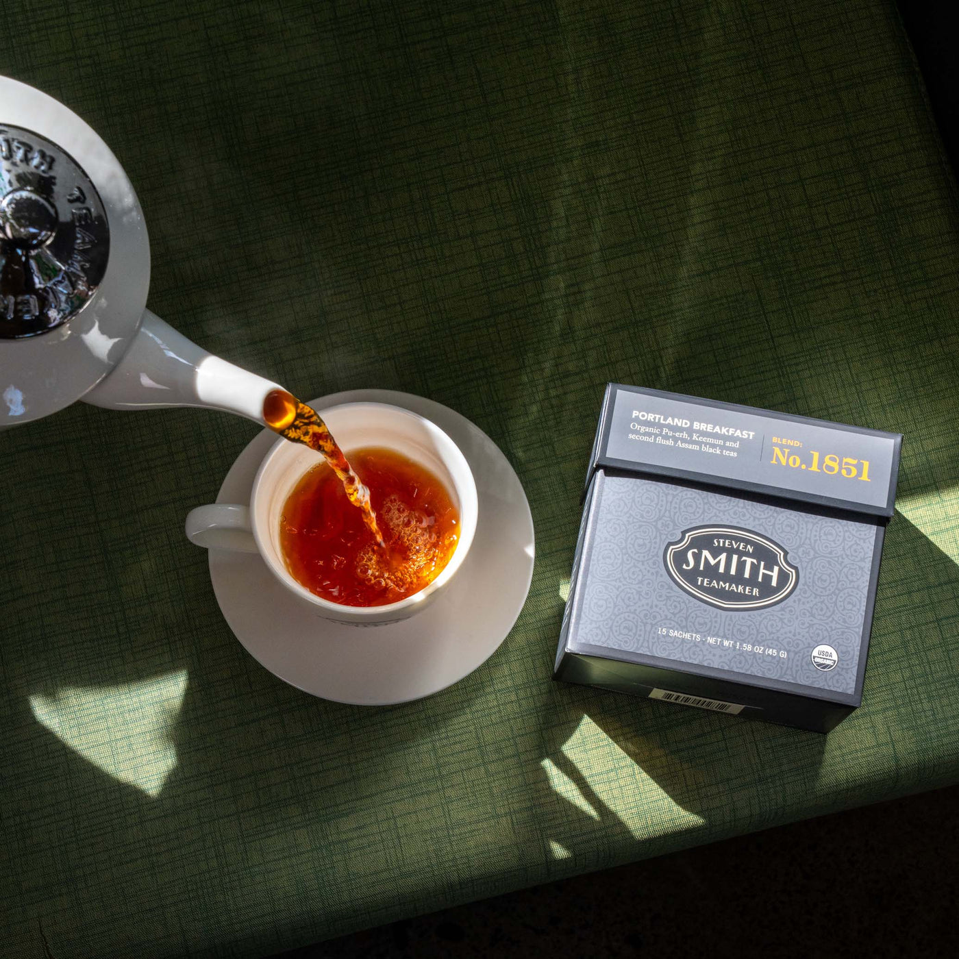 Tea being poured into a cup with a 'Smith' tea box on a green surface