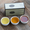 Dark silver box with black trim on wooden background next to three cups of tea in porcelain cups..