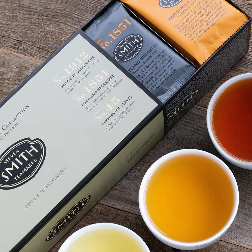 Dark silver box with black trim slightly opened to display orange and black tea sachets inside.